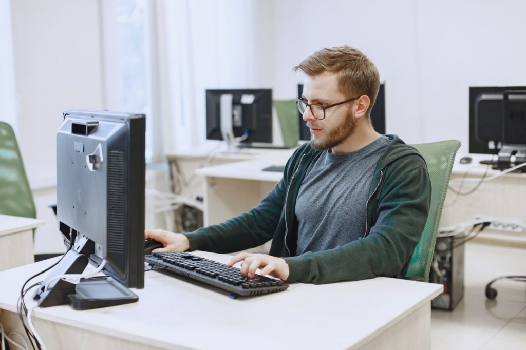 a-man-wearing-eyeglasses-while-looking-at-the-computer-5621968 Young man with eyeglasses working on a desktop computer in a modern office environment.