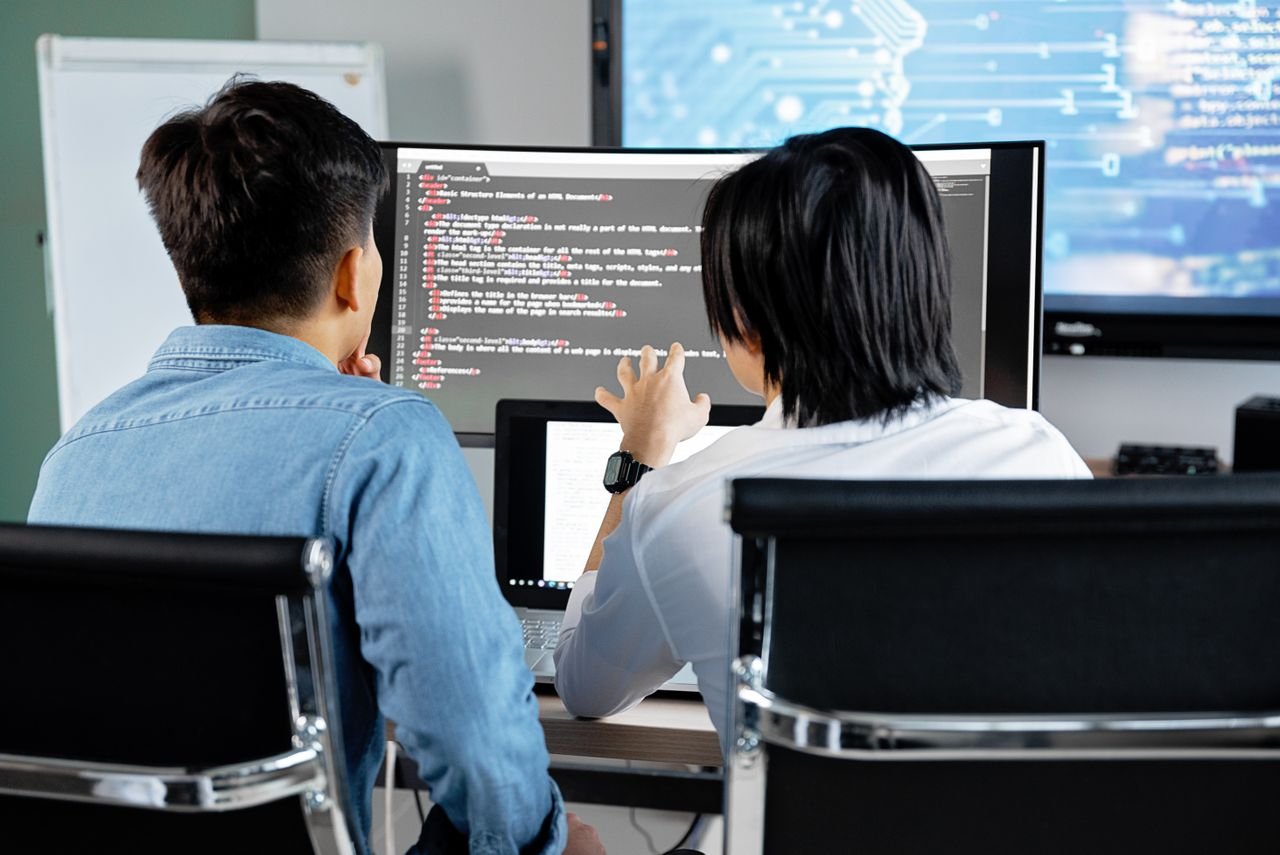service-05 Two developers working together in an office, discussing code on a screen. Technology teamwork setting.